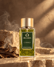 A bottle of Okaasha Canali Extrait de Parfum stands on a stone surface with warm golden lighting and smoke in the background.
