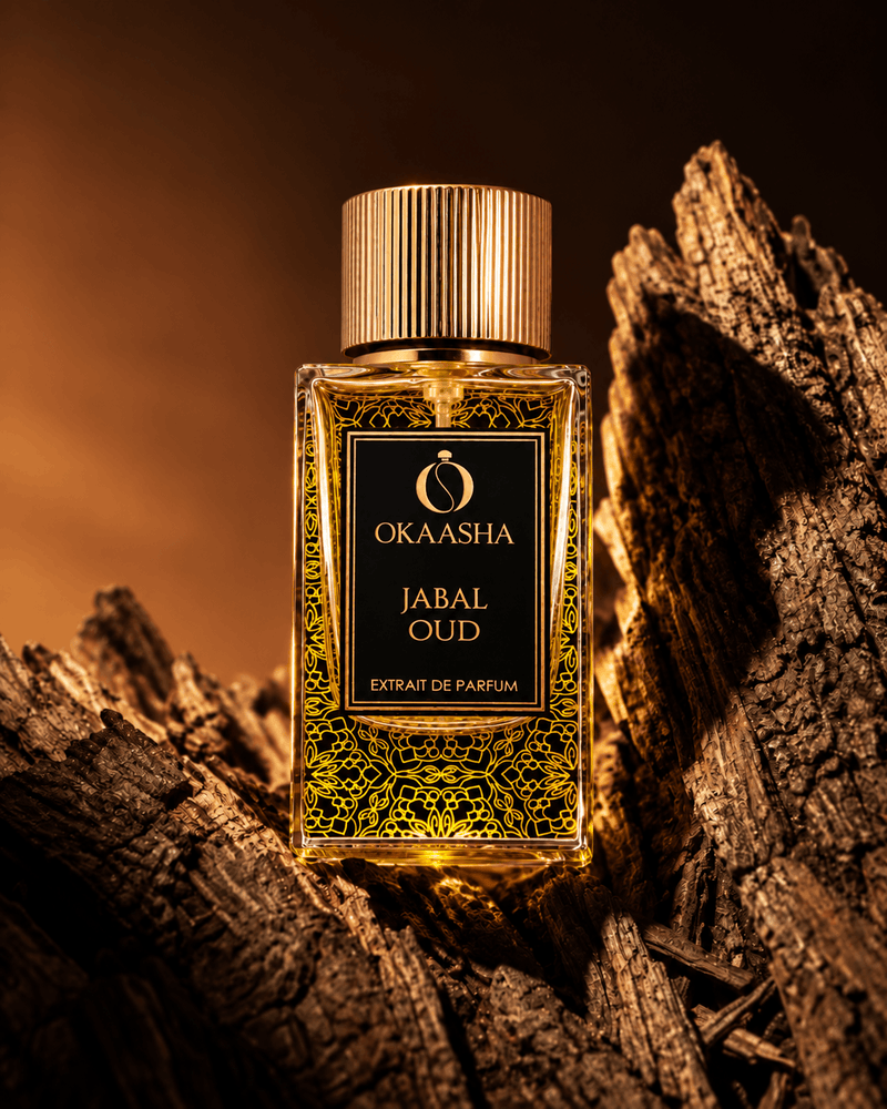 A bottle of Okaasha Jabal Oud extrait de parfum stands on textured wood logs against a warm, dark brown background.